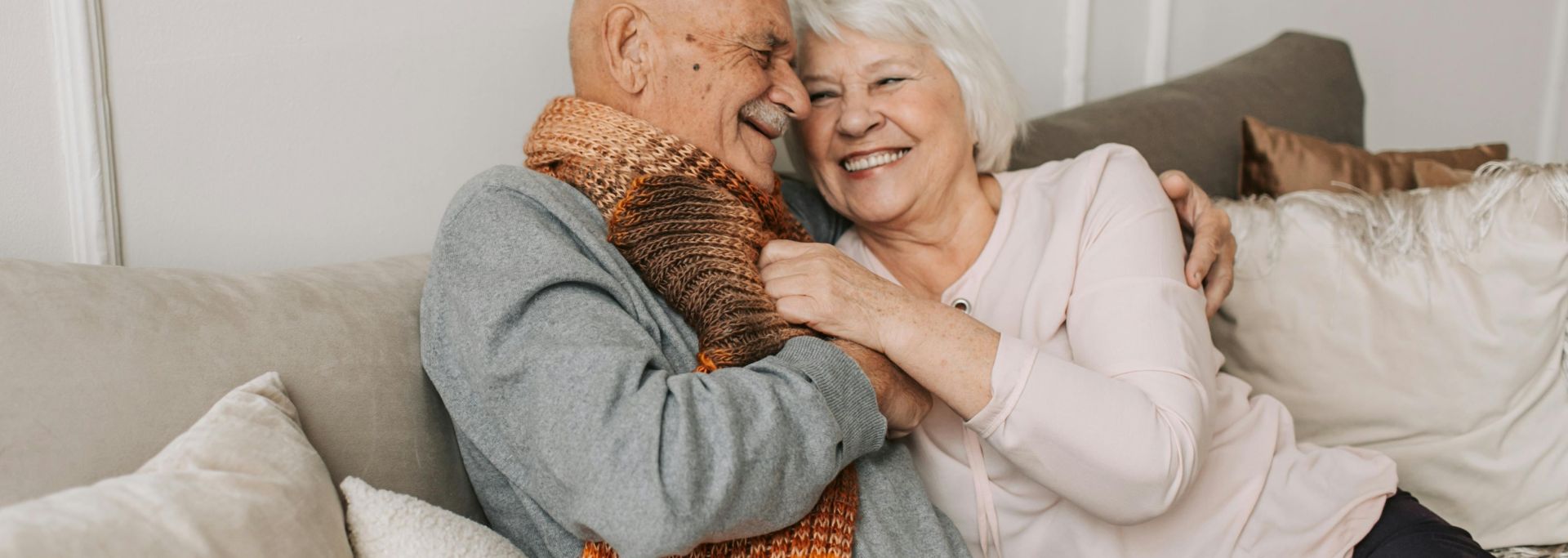 Happy elderly couple embraced in a cozy home setting, sharing joyful smiles.