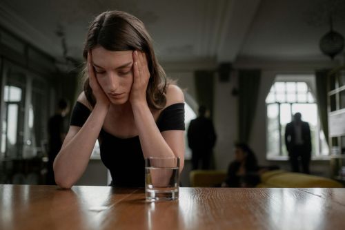 A sad woman in a black dress with a glass of water, indoors.