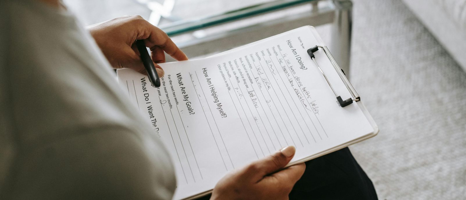 From above of blurred anonymous female psychologist reading documents on clipboard while sitting in office near table during session